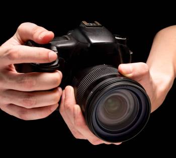 Male hand holding a digital camera on a black background.